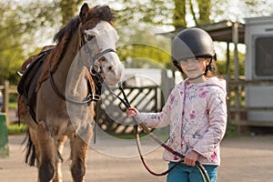 Young girl wearing riding helmet leading Welsh pony