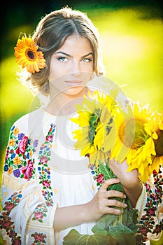 Young girl wearing Romanian traditional blouse holding sunflowers outdoor shot. Portrait of beautiful blonde girl with sunflowers