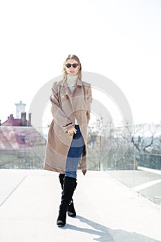 Young girl wearing sunglasses with long blonde hair in the wind, wearing a long coat outside