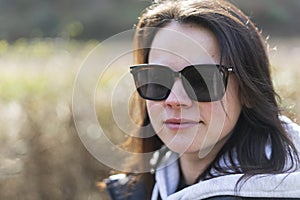 The young girl wearing sunscreen glasses smiles in her jacket and sweater on the street