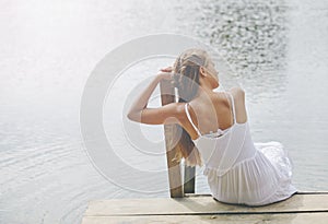 Young girl wearing a white sitting by the river in summer afternoon.