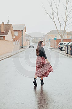 Young girl wetting her skirt and smiling in the rain with black boots and printed long skirt