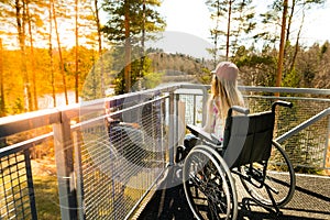 Young girl in a wheelchair on a balcony looking at the nature in