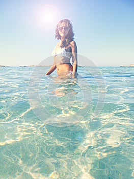 Young girl in white bikini into the clear water of sea against blue sky in sunny day. Cool girl enjoying the holiday at caribbean