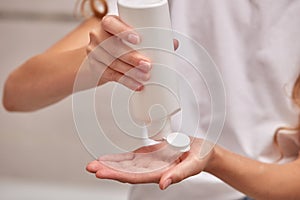 A young girl with a white bottle puts liquid soap on her hands.