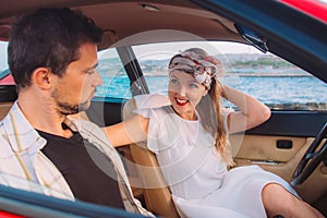 Young girl in white dress and man sitting on the front seats of the red car