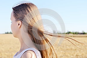 Young girl in the white dress stands in the field and wind flutters her hair