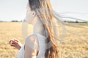 Young girl in the white dress stands in the field and wind flutters her hair