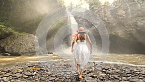 Young Girl in White Dress and Straw Hat Runing to Tegenungan Waterfall and Raising Up Arms. Carefree Lifestyle Travel 4K