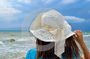 Young girl in a white hat on the sea beach. Clean, sandy beach against the blue sea