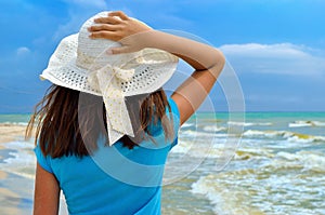 Young girl in a white hat on the sea beach. Clean, sandy beach against the blue sea