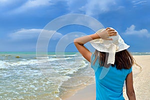 Young girl in a white hat on the sea beach. Clean, sandy beach against the blue sea