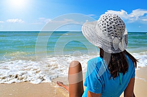 Young girl in a white hat on the sea beach. Clean, sandy beach against the blue sea