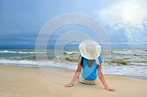 Young girl in a white hat on the sea beach. Clean, sandy beach against the blue sea