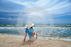 Young girl in a white hat on the sea beach. Clean, sandy beach against the blue sea