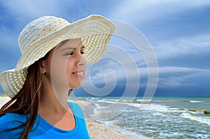 Young girl in a white hat on the sea beach. Clean, sandy beach against the blue sea