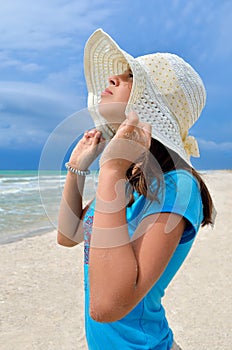 Young girl in a white hat on the sea beach. Clean, sandy beach against the blue sea