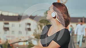 A young girl in white headphones with pleasure listens to music on a warm summer evening.