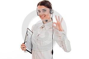 Young girl in white shirt and headphones with microphone smiles into the camera and looks hand gesture