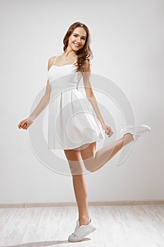 Young girl in white short dress spinning around. Dynamic studio photoshot