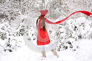 A young girl in a white sweater and a red knitted hat and a flying scarf looks away and waves her hand against the background of a