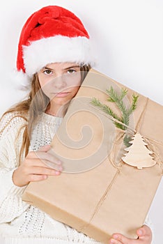 Young girl in white sweater and red santa hat holds present christmas direct look