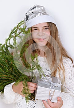 Young girl in white sweater and silver santa hat holds present and christmas tree branches close