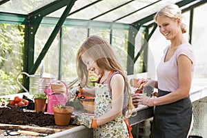 Young girl and woman in greenhouse putting