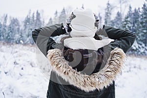 Young girl, woman in knitted mittens lost in forest woman holding her head.Walking in beautiful winter forest among trees,firs,