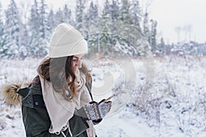 Young girl, woman with mobile phone walks in beautiful winter forest among trees, firs, covered with snow. Magnificent nature and