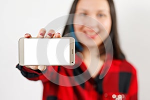 A young girl woman in a red and black shirt is holding a smartphone with a blank white screen horizontally in front of her