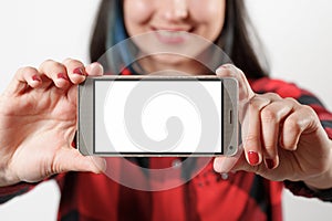 A young girl woman in a red and black shirt is holding a smartphone with a blank white screen horizontally in front of her