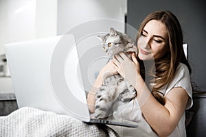 Young Girl Works at Home with a Computer and Hug Cat