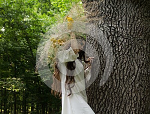 Young girl in wreath walks in forest. Folk style.