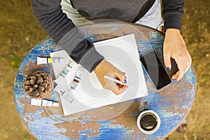 Young girl writes in a notebook with cell phone, cup of coffee a