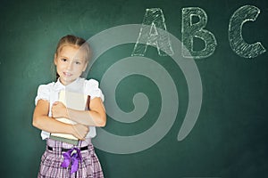 Young girl writing ABC on green chalkboard