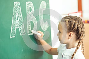 Young girl writing ABC on green chalkboard