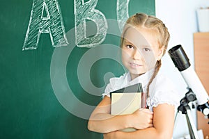 Young girl writing ABC on green chalkboard