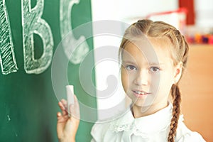 Young girl writing ABC on green chalkboard