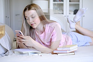 A young girl 15-18 years old lies on the bed with a phone in her hands.