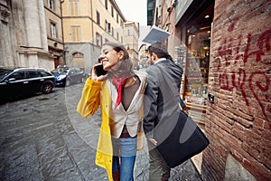 A young girl in a yellow raincoat bumped into a passerby while talking on the smartphone and walking the street on a rainy day.