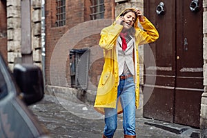 A young girl in a yellow raincoat is having a phone call while walking the city on a rainy day. Walk, rain, city