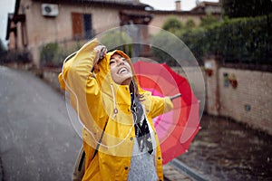 A young girl in a yellow raincoat and with pink umbrella who is walking the street is in a good mood while enjoying music and rain