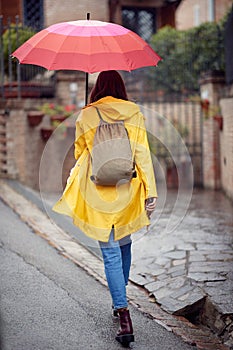 A young girl in a yellow raincoat is walking on the street during a rainy day. Walk, rain, city