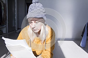 A young girl in a yellow sweater and two hats is horrified to study large bills, taxes and utility bills.