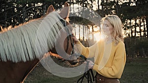 Young girl in yellow sweather hugs the sweet male brown horse in the wood slow motion