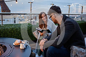 Young girlfriend reading for boyfriend while couple resting at roof top cafe
