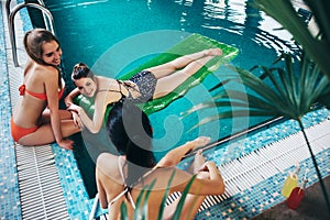 Young girlfriends wearing swimwear relaxing in swimming-pool talking and smiling