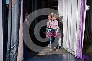 Young girls - athletes are preparing for the show, many young cheerleaders are standing on stage behind the curtain, sportsmen are