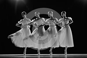Young girls, ballerinas in white tutus with blue bows dancing in motion on stage. Monochrome photo with motion blur